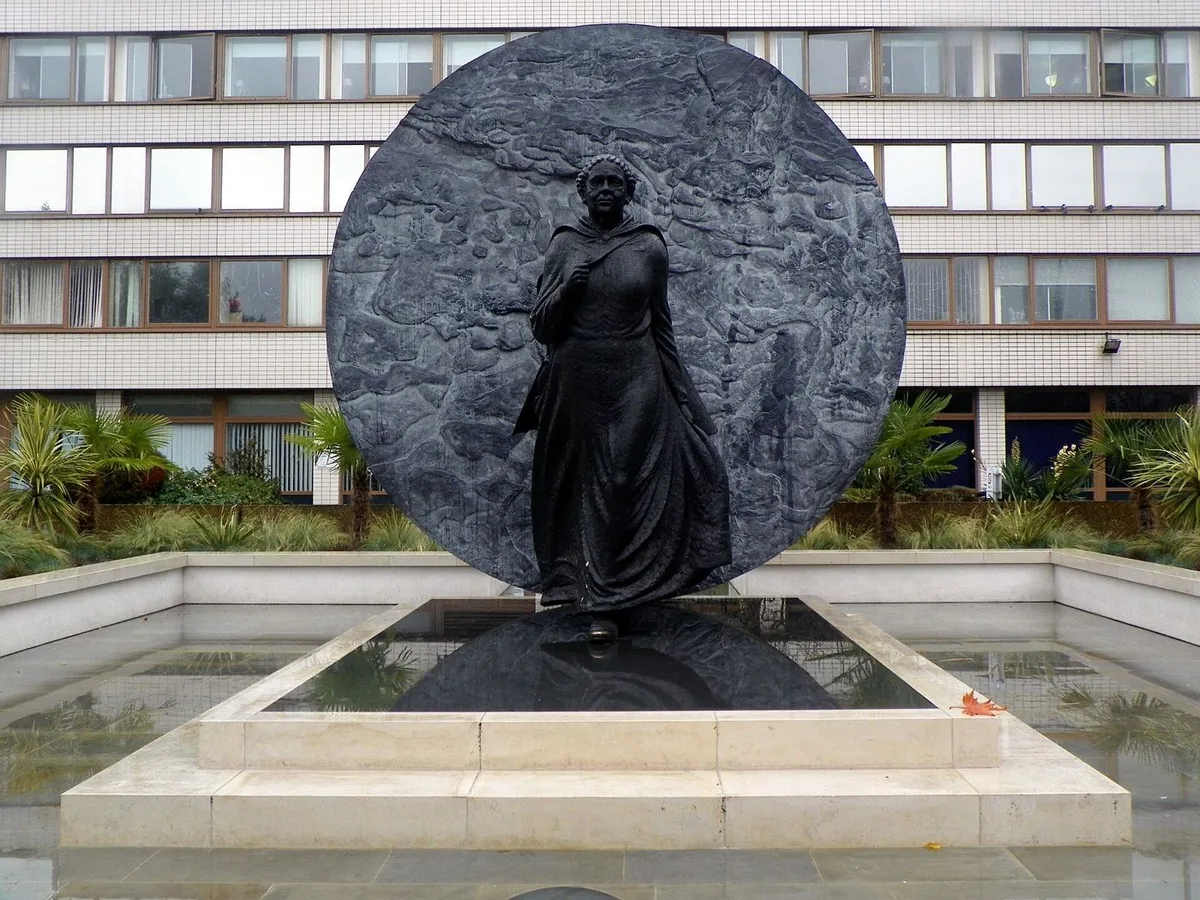 Bronze statue of Mary Seacole striding forward in front of a large bronze disc outside St Thomas’ Hospital.